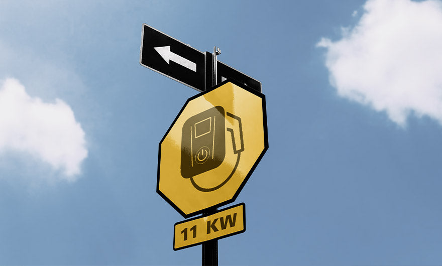 Ein gelbes Straßenschild mit einem Ladesteckersymbol und darunter 11 KW ist auf einem Mast mit einem Pfeil nach links vor einem blauen Himmel mit Wolken montiert.
