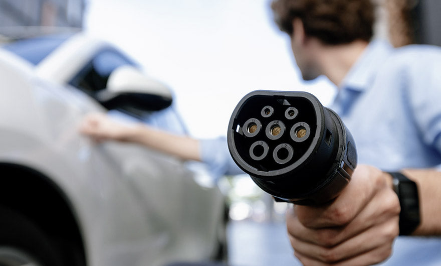 Eine Person hält einen Ladestecker für Elektrofahrzeuge in die Nähe eines weißen Autos und bereitet sich darauf vor, es anzuschließen.