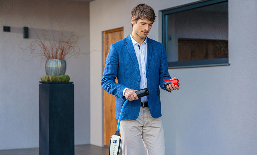Ein Mann in einem blauen Blazer steht draußen und hält ein Ladekabel für ein Elektrofahrzeug in der Hand, um es anzuschließen.