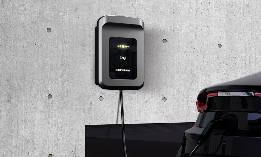 Ein schwarzes Elektroauto ist an eine an der Wand befestigte Ladestation an einer Betonwand angeschlossen.