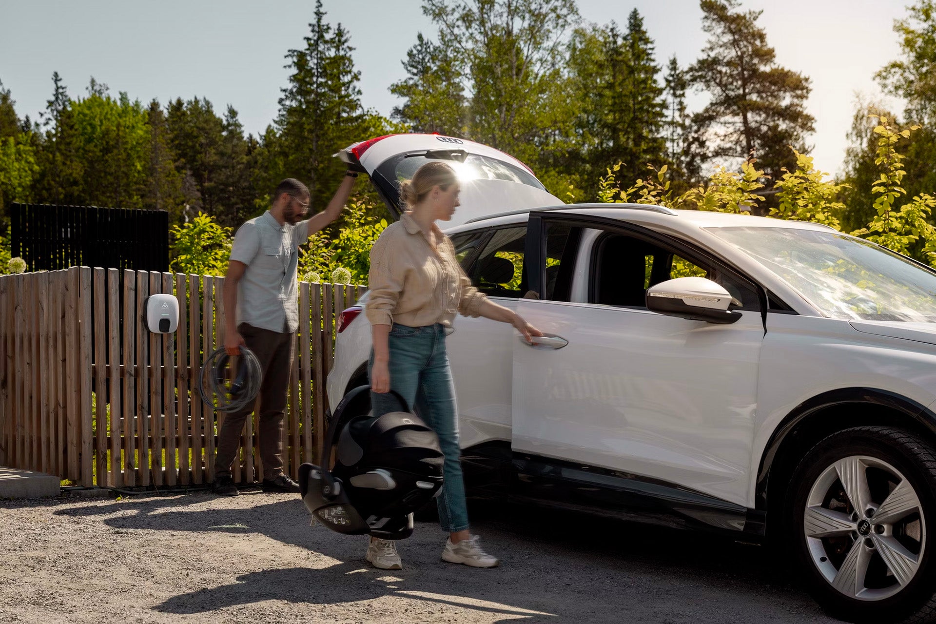 Eine Frau öffnet die Vordertür des weißen Elektroautos mit Kindersitz, während ein Mann ein Charge Amps Luna Kabel neben dem Ladegerät hält und so zukunftssicheres Laden mit integriertem Lastenausgleich von Charge Amps ermöglicht.