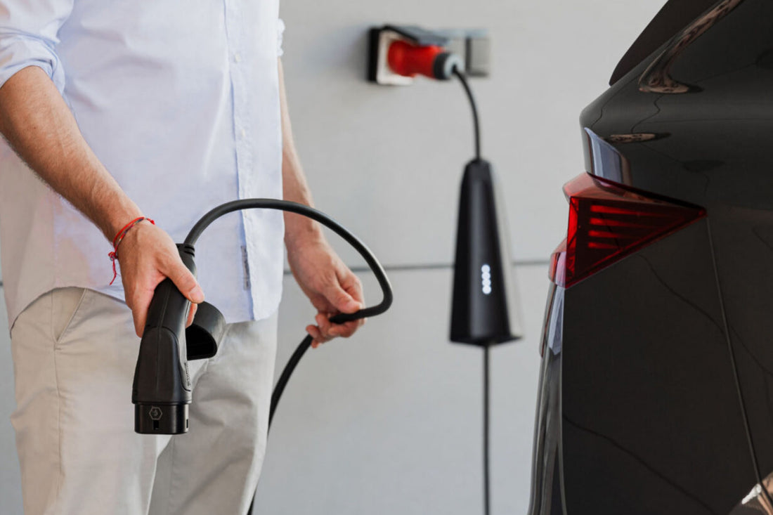 Eine Person hält ein Ladekabel neben einem schwarzen Elektroauto, das neben einem wandmontierten NEcharge One von NEcharge geparkt ist und bequemes 3-Phasen-Laden ermöglicht.