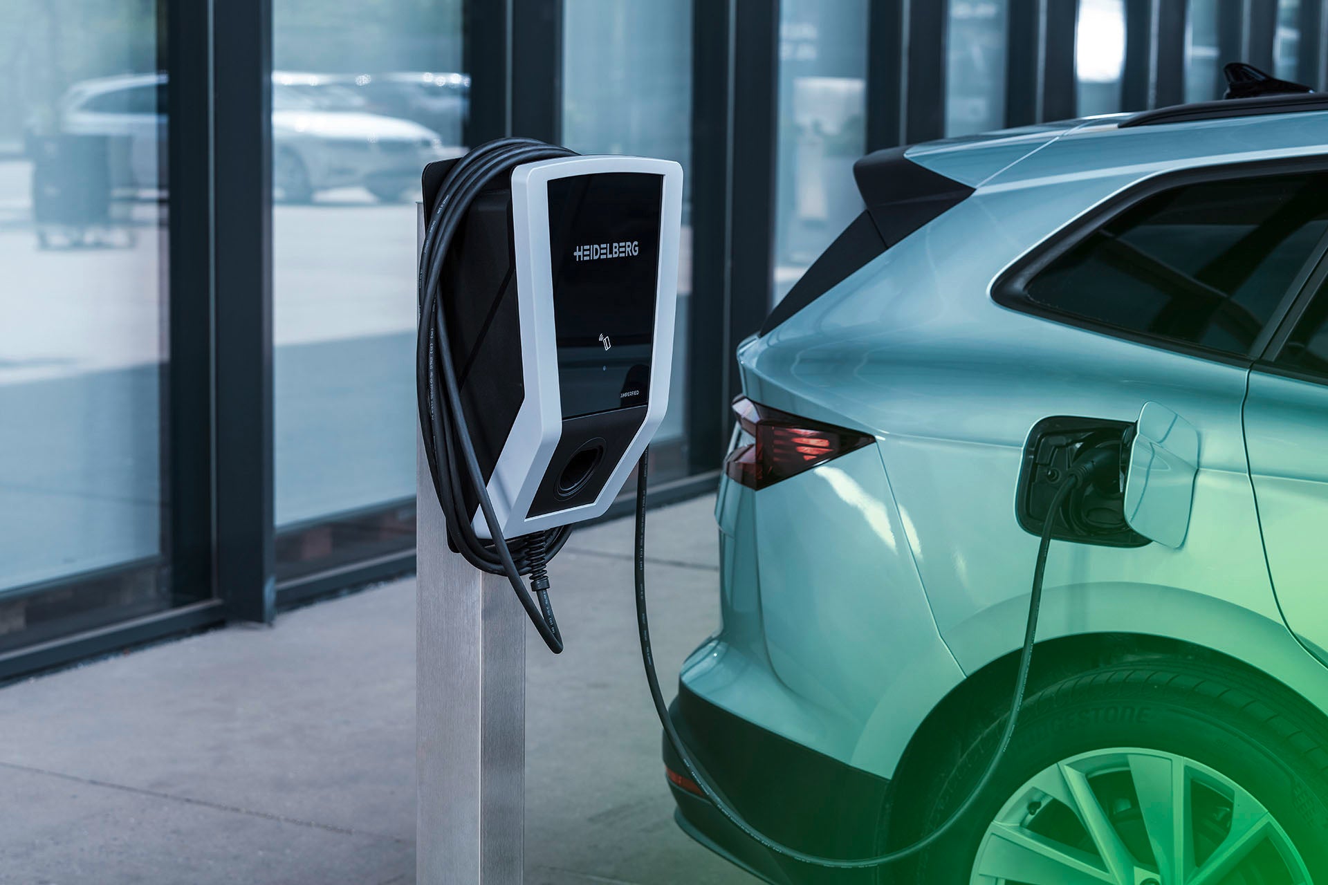 Ein silbernes Elektroauto ist an einer Heidelberg AMPERFIED Wallbox connect.business in einem modernen Gebäude mit großen Fenstern geparkt und wird aufgeladen, was das fortschrittliche Energiemanagement von Heidelberg AMPERFIED unterstreicht.