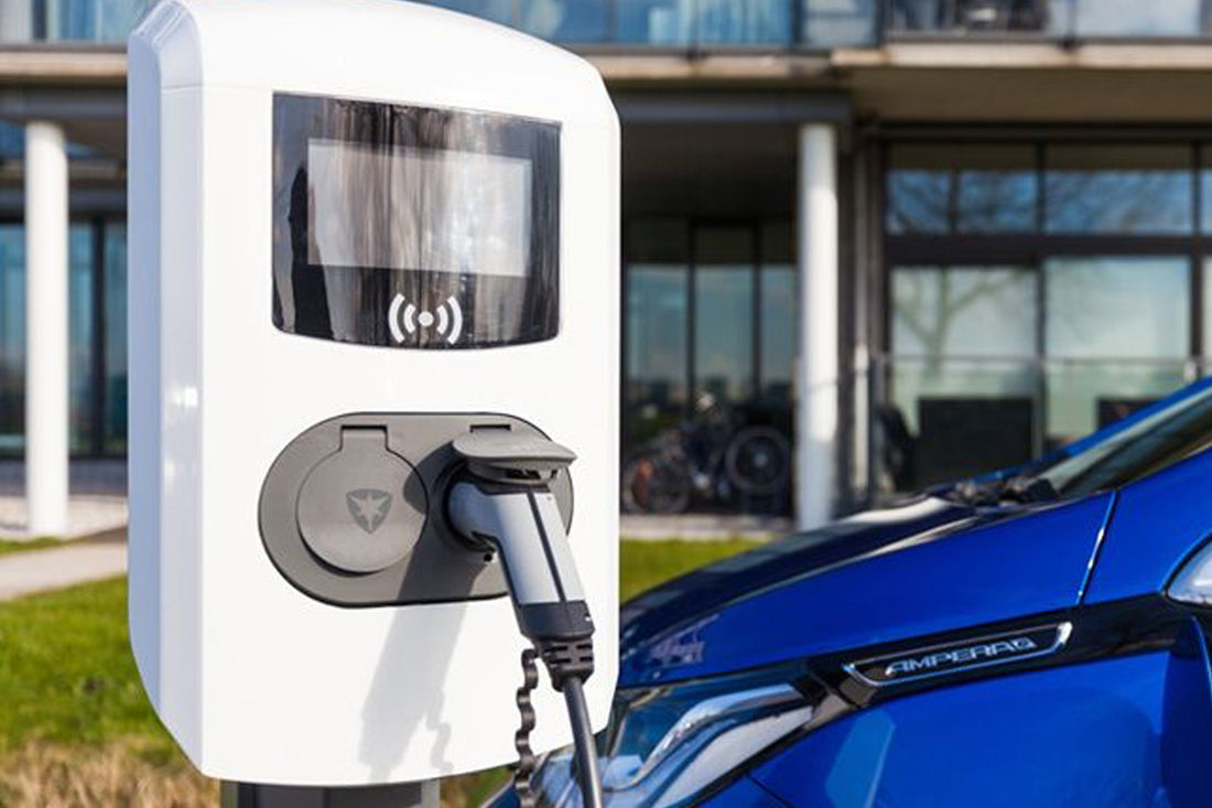 Ein blaues Elektroauto ist an einer Alfen Eve Double Pro-Line, einer weißen intelligenten Doppelladestation von Alfen, an einer öffentlichen Ladestation im Freien angeschlossen, im Hintergrund sind ein Gebäude und ein Fahrrad zu sehen.