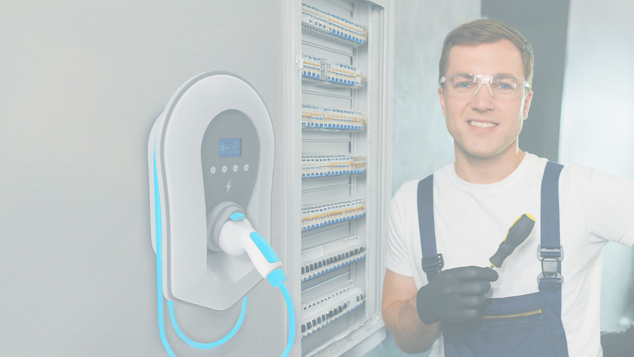 Ein Elektriker mit Schutzbrille und Handschuhen steht neben einer Ladestation für Elektrofahrzeuge, die an einer Wand in der Nähe eines offenen Schaltschranks montiert ist.