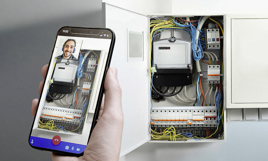 Eine Hand hält ein Smartphone mit einem Videoanruf, der auf einen geöffneten Schaltkasten gerichtet ist – ideal für die Fernunterstützung mit dem e-mobilio Video-Installations-Check des e-mobilio Shops bei der Beratung zur Elektroinstallation oder Wallbox-Installation.