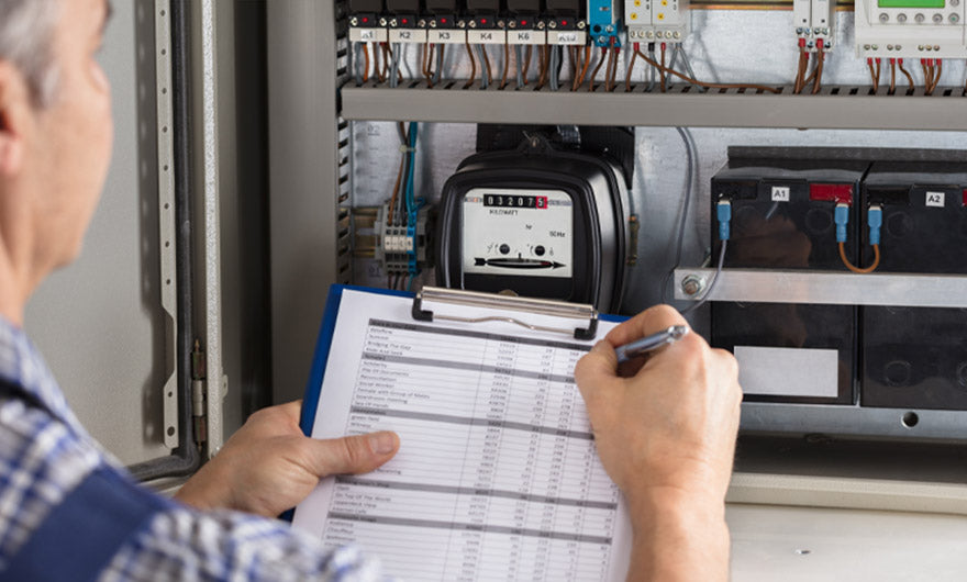 Eine Person trägt vor einem offenen Schaltschrank Zählerstände in eine Checkliste ein – perfekt für den e-mobilio Vor-Ort-Installations-Check vom e-mobilio Shop oder andere Elektroinstallationen.