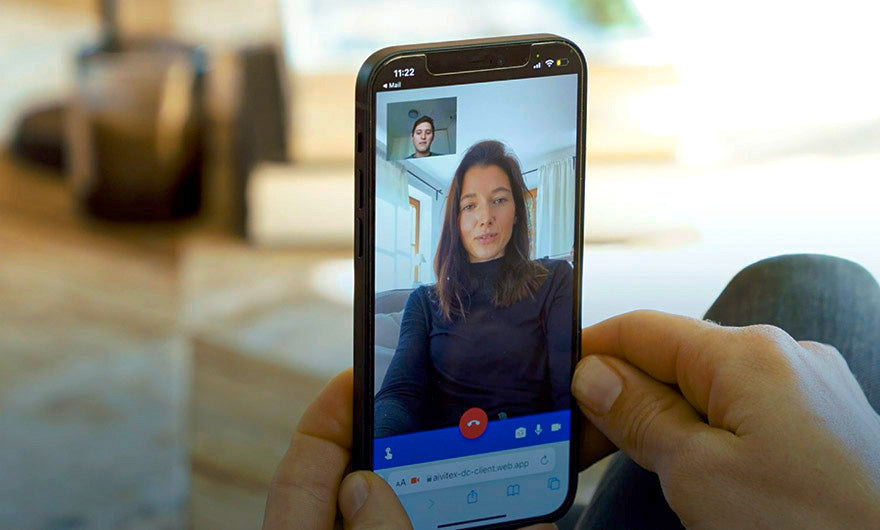 Eine Person hält ein Smartphone in der Hand, auf dem ein Videoanruf über den e-mobilio Shop läuft, bei dem zwei Personen ihren letzten e-mobilio Video-Installations-Check besprechen.