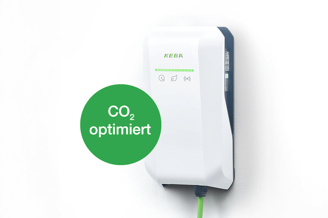Eine weiße KEBA KeContact P40 Ladestation ist an der Wand montiert und verfügt über Kontrollleuchten und ein grünes Kabel mit einem grünen Kreis mit der Aufschrift „CO₂ optimiert“ für Elektrofahrzeuge.