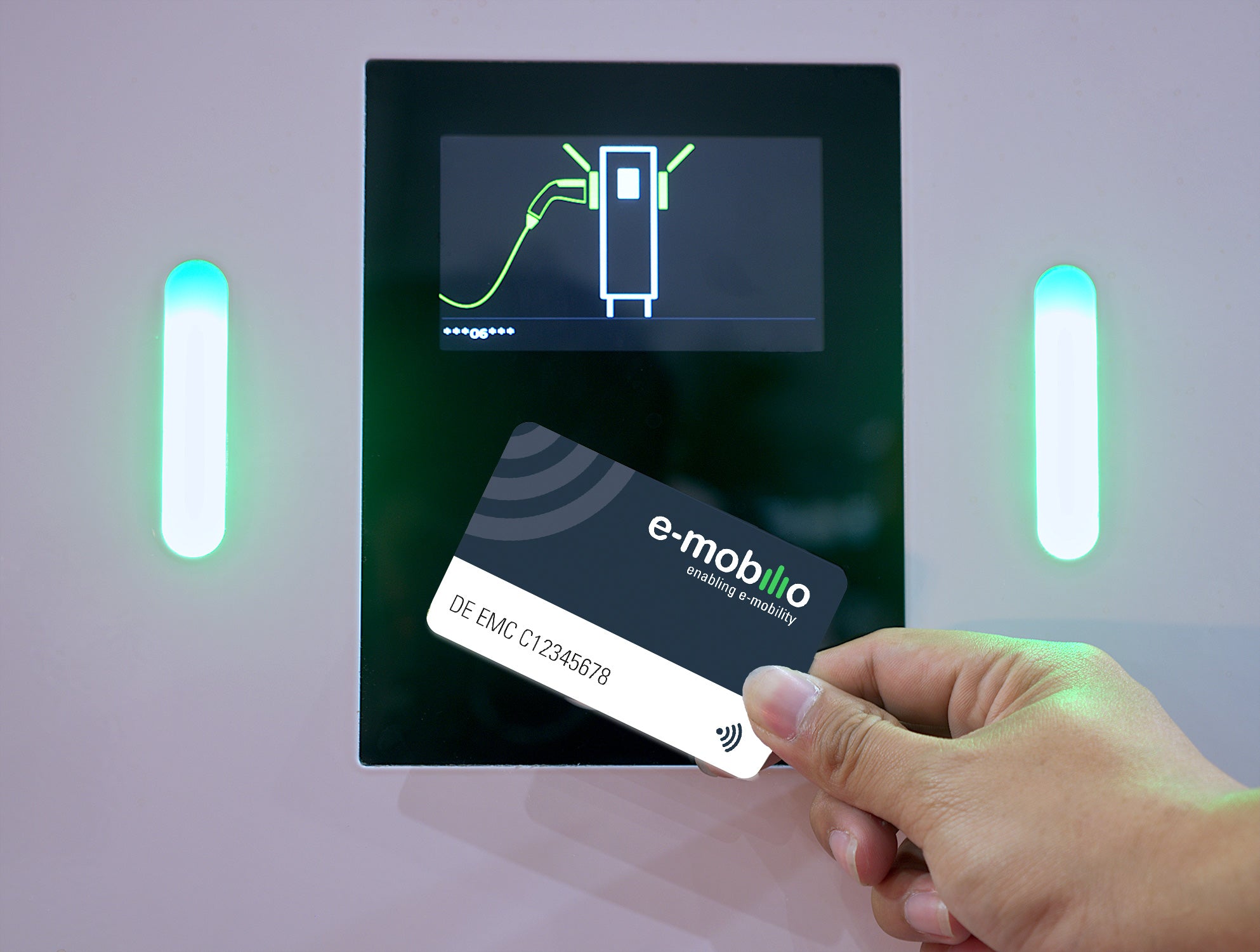 Eine Hand hält die e-mobilio Ladekarte aus dem e-mobilio Shop neben dem Bildschirm einer Ladestation für Elektrofahrzeuge, auf dem ein Ladesymbol angezeigt wird.