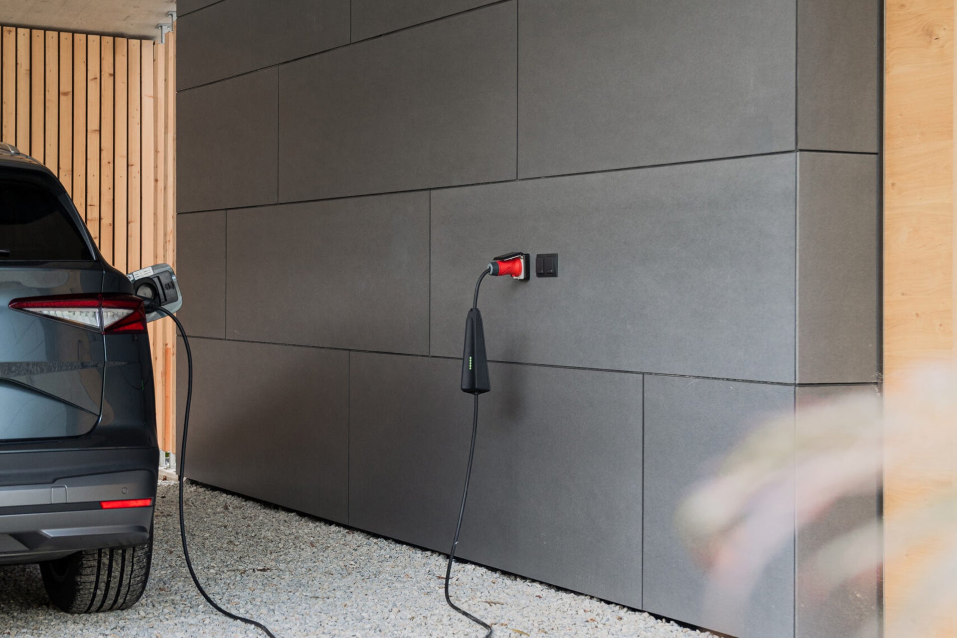 Ein Elektrofahrzeug wird am NEcharge One von NEcharge geparkt und aufgeladen, einer wandmontierten mobilen Ladestation in einer modernen Garage mit Kiesboden, die effizientes 3-Phasen-Laden unterstützt.