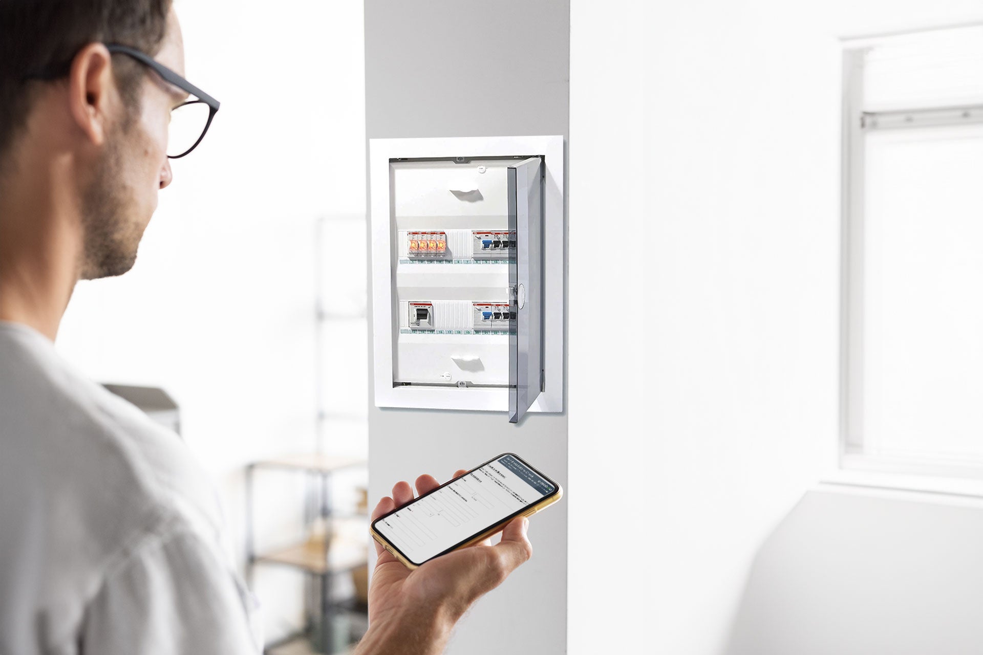 Eine Person mit einem Smartphone überprüft einen geöffneten Schaltschrank und nutzt dabei ggf. den e-mobilio Selbst-Installations-Check aus dem e-mobilio Shop, um ihre Ladeeinrichtung zu bewerten.