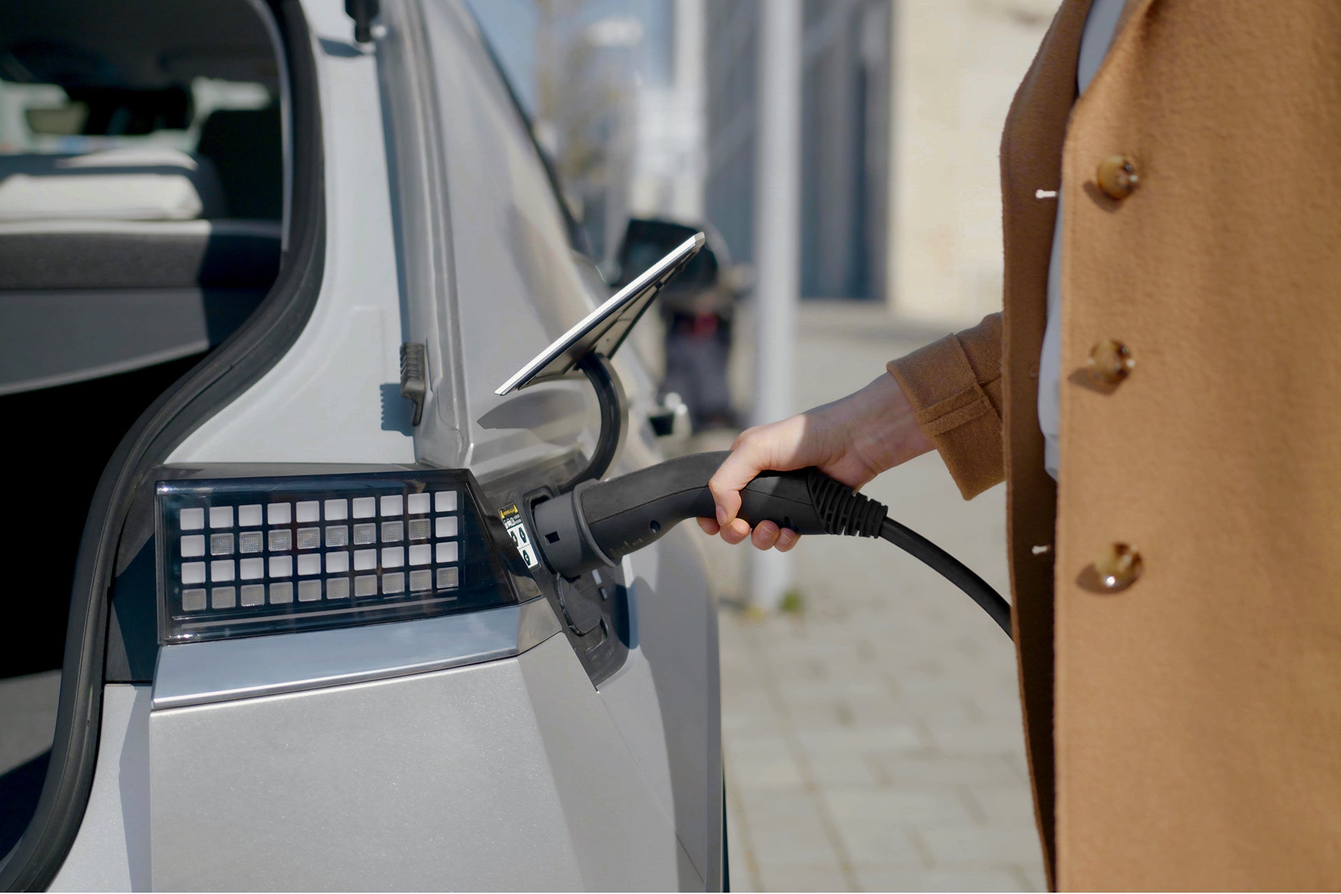 Eine Person im braunen Mantel steckt auf einer asphaltierten Straße ein Lapp-Ladekabel Typ 2 von LAPP in ein Elektroauto und demonstriert so den Komfort des Ladens von Elektroautos.