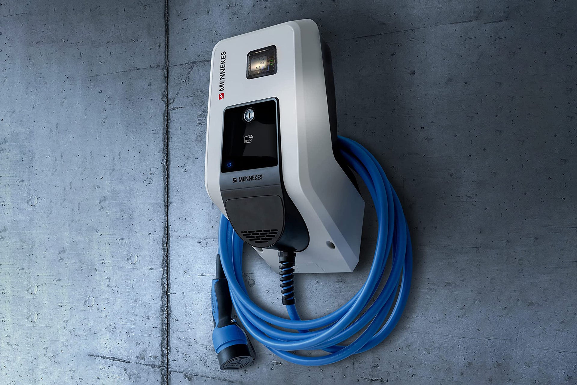 Die Mennekes AMTRON® Professional, eine wandmontierte Ladestation für Elektrofahrzeuge von Mennekes, ist mit einem blauen Spiralkabel an einer grauen Betonwand installiert und verfügt über eine RFID-Autorisierung für sicheren Zugang.