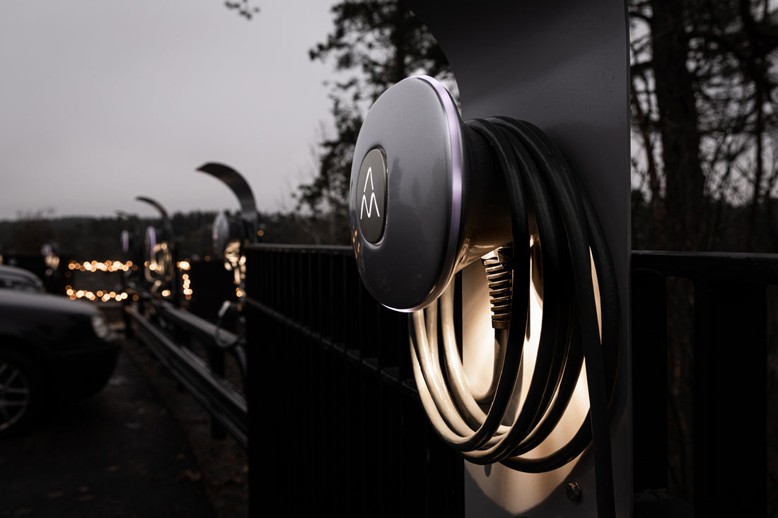 Eine Nahaufnahme der Charge Amps Halo-Ladestation von Charge Amps mit Spiralkabel, montiert auf einem Mast im Freien in der Nähe eines Parkplatzes und aus recyceltem Aluminium gefertigt.