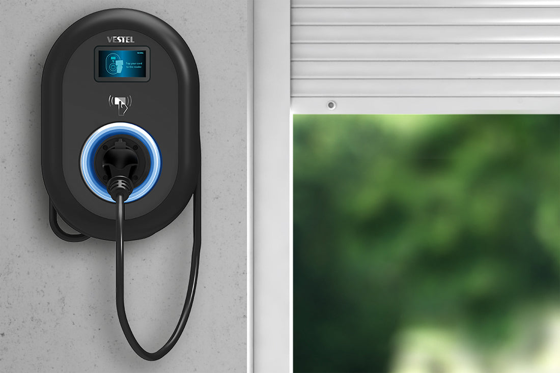 Eine wandmontierte Ladestation Vestel EVC04 Connect Plus 22 kW ist mit einem eingesteckten Stecker neben einem Fenster abgebildet, draußen ist verschwommenes Grün zu sehen.