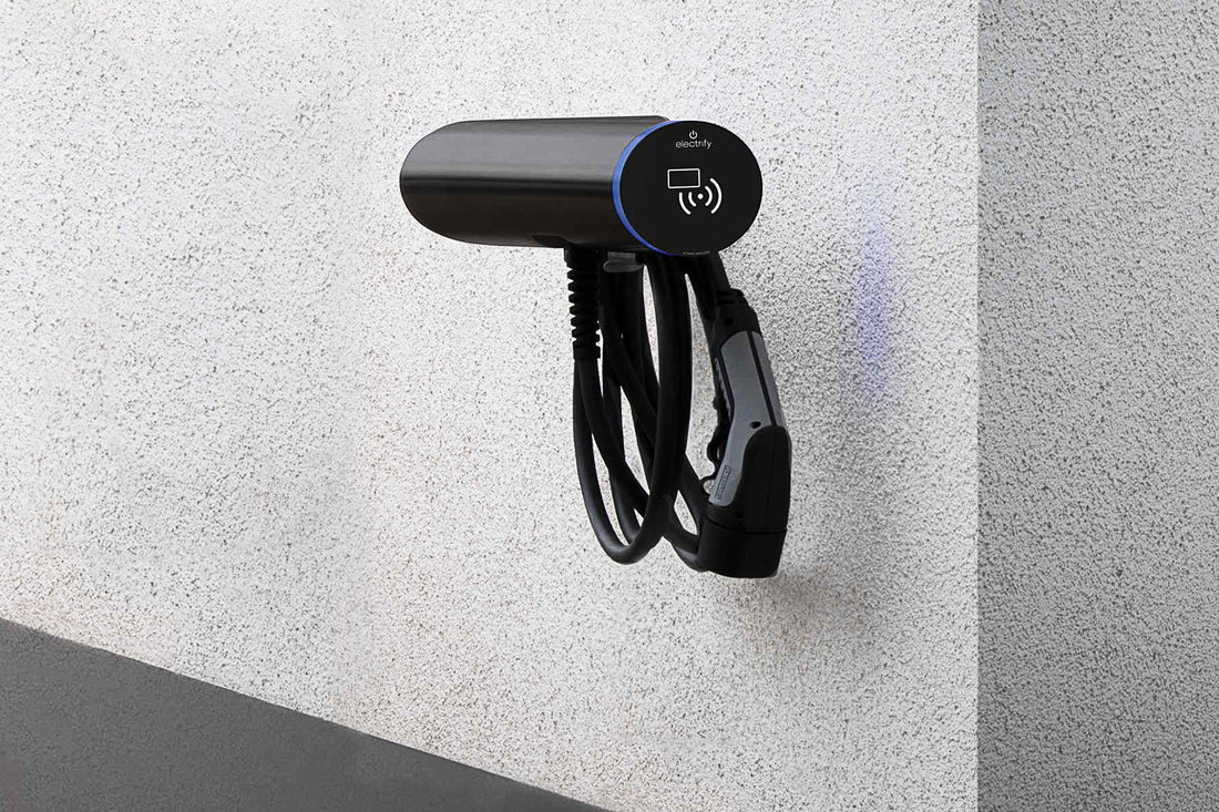 Eine schwarze Ladestation für Elektrofahrzeuge von Hesotec electrify eBox wr30 Base ist an einer strukturierten weißen Wand montiert. Das Kabel ist ordentlich aufgewickelt und bietet eine bequeme App-Steuerung.