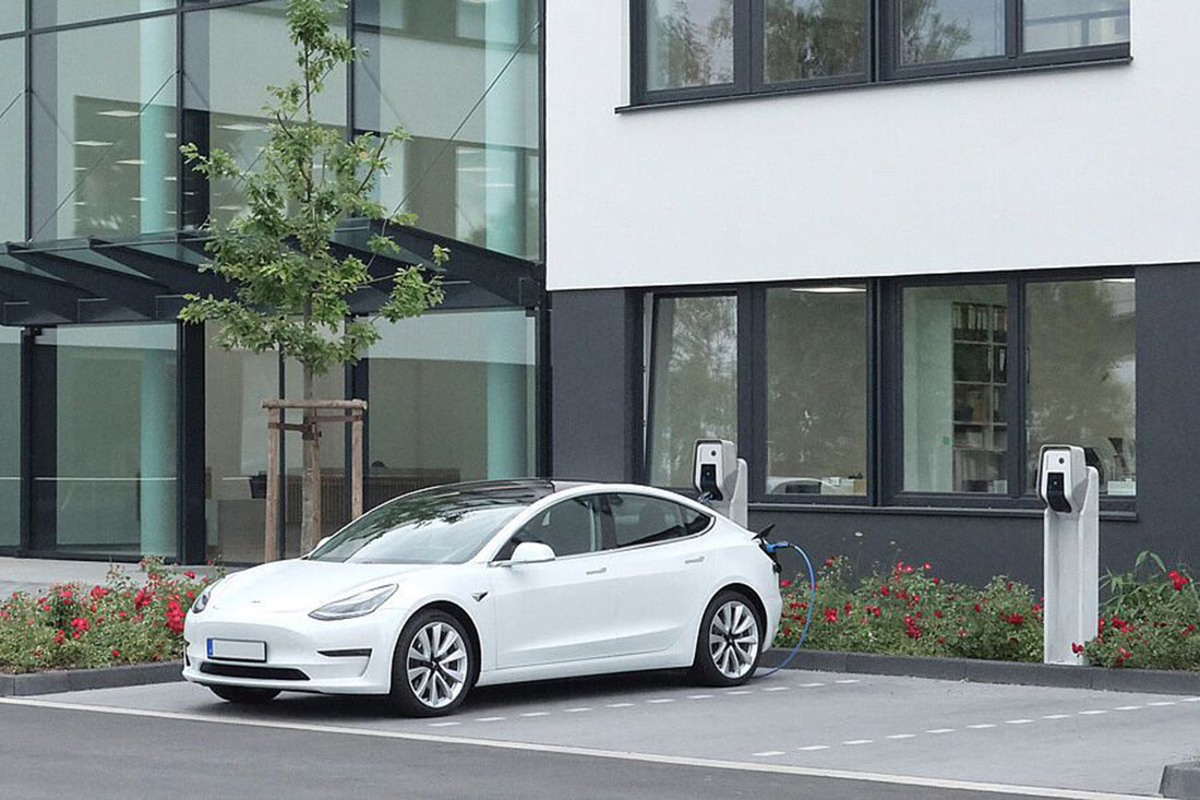 Ein weißes Elektroauto parkt neben einem modernen Gebäude und wird an einer Mennekes AMTRON® Professional-Station mit RFID-Autorisierung und nahtloser Integration in Energiemanagementsysteme aufgeladen.