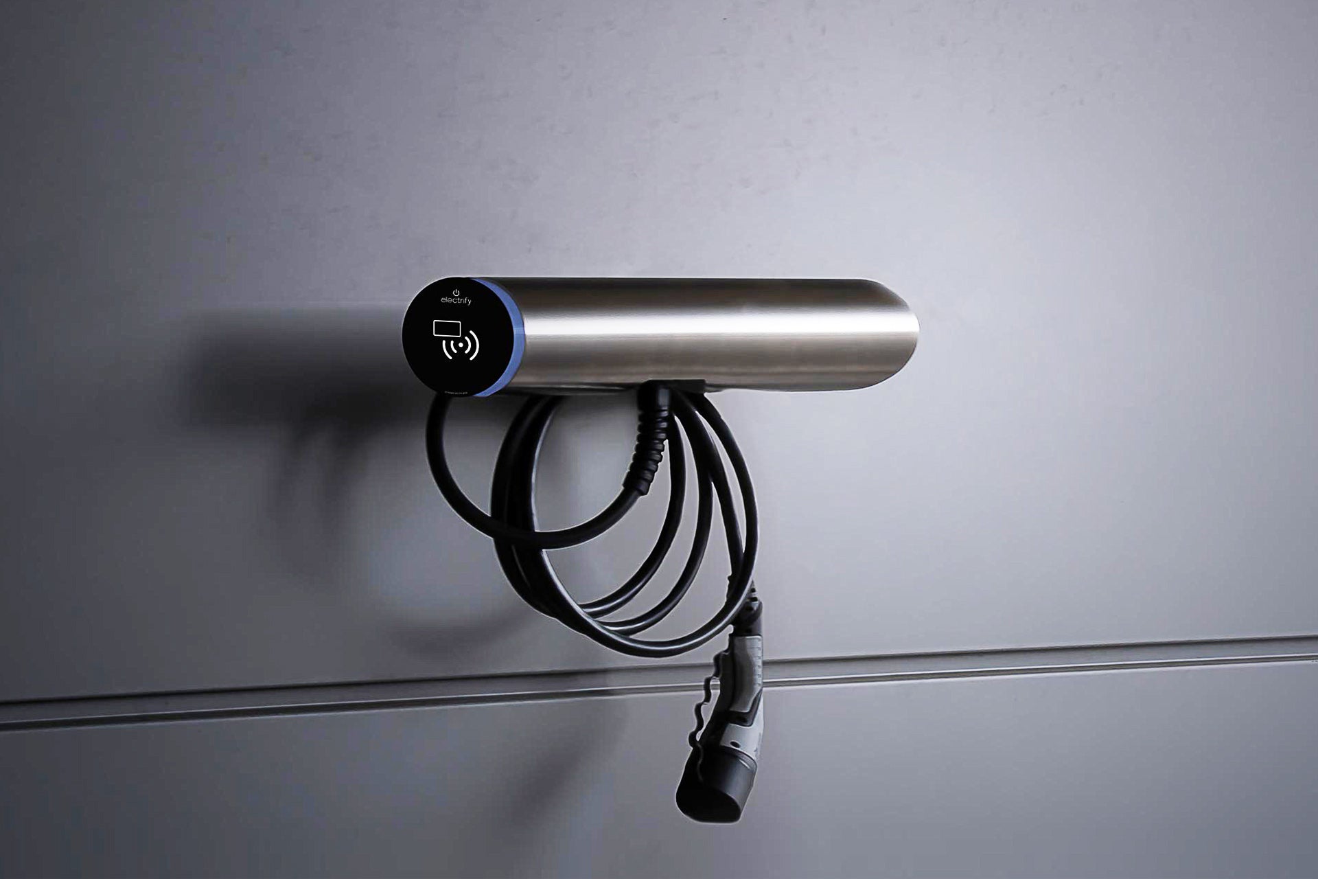 Die wandmontierte Hesotec electrify eBox wr30 Base verfügt über ein zylindrisches Metallgehäuse, ein Spiralladekabel und eine App-Steuerung zum bequemen Laden von Elektrofahrzeugen.