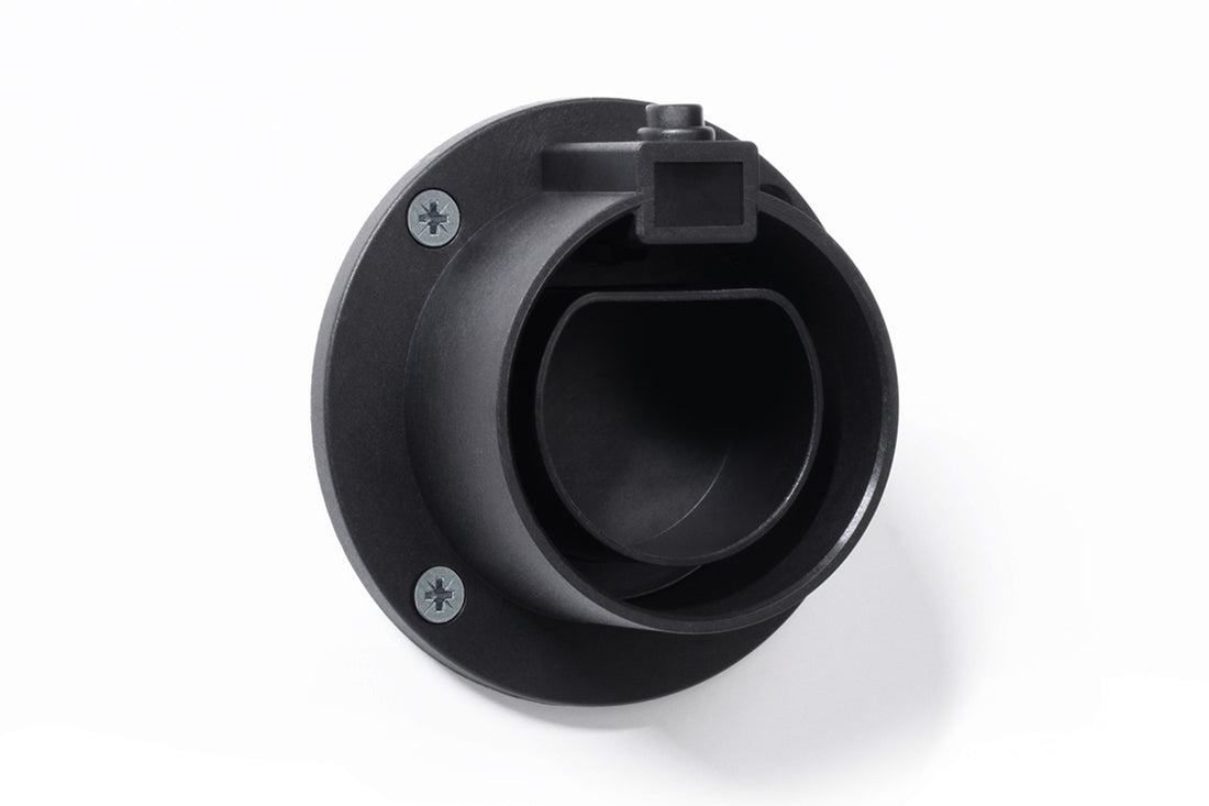 Die ELECTRIC-WAYS Steckerhalterung Typ 2 von ELECTRIC-WAYS ist eine schwarze runde Wandhalterung aus Kunststoff für die Wandmontage mit einer offenen zylindrischen Halterung für Ladestecker Typ 2 und einer rechteckigen Kerbe an der Oberseite, die mit zwei Schrauben auf weißem Hintergrund dargestellt ist.